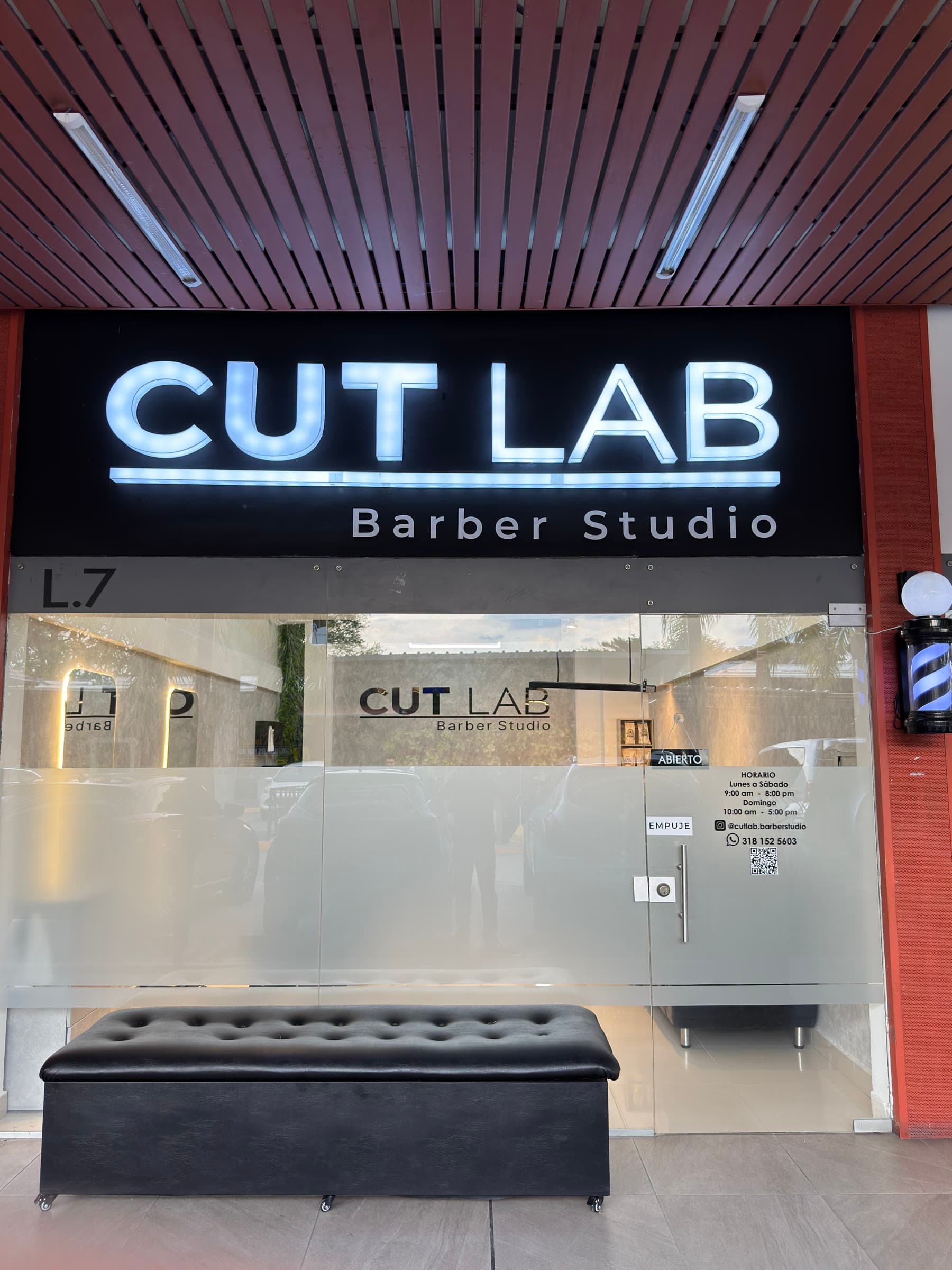 Fachada de CUT LAB Barber Studio, con el letrero iluminado y la butaca de espera